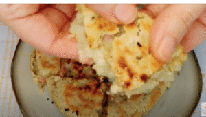 una mano muestra un trozo del pan de bacon y queso