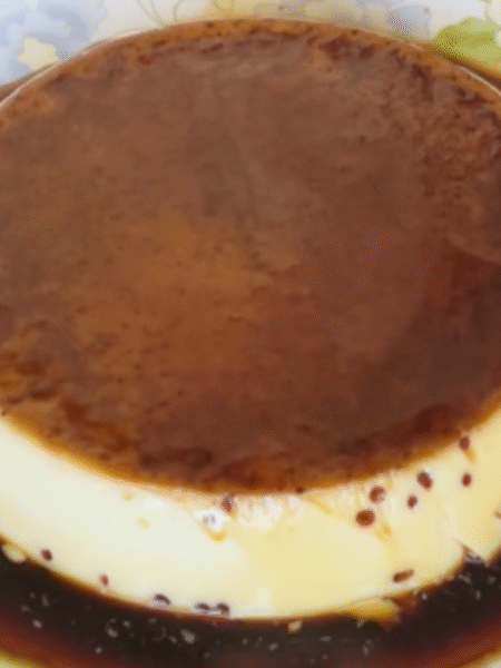 flan redondo cubierto de caramelo dorado en plato de ceramica con flores