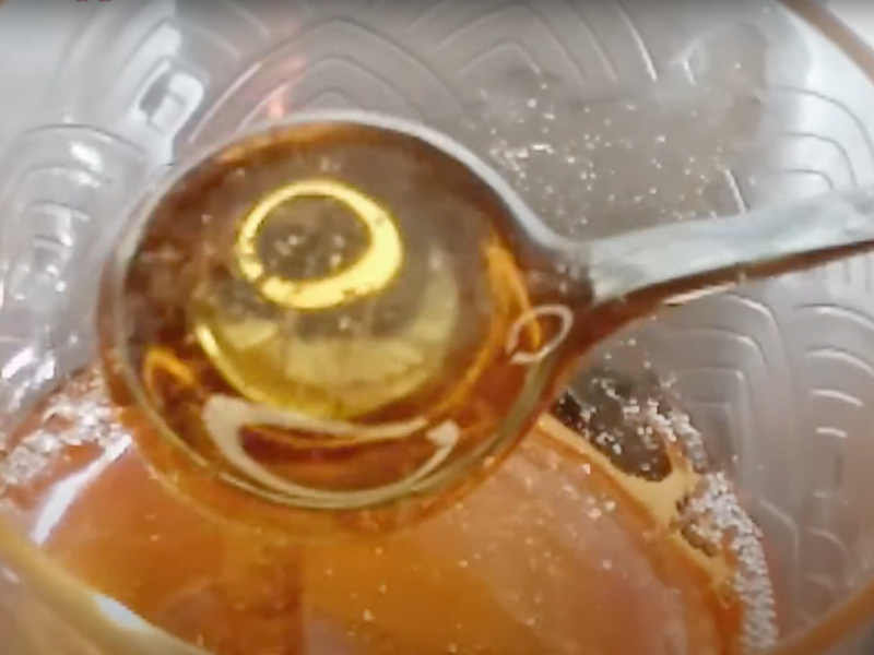 se toma una cucharada de miel de manzana mostrando su color ámbar, brillo cristalino y viscosidad similar a la miel de abejas